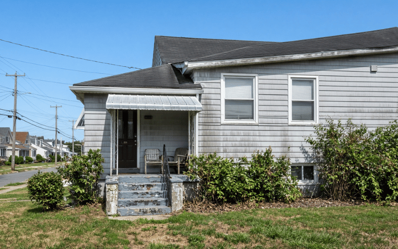 Gray single-story Long Island house with a metal porch awning and worn concrete steps, sold while a judgment lien is cleared at closing